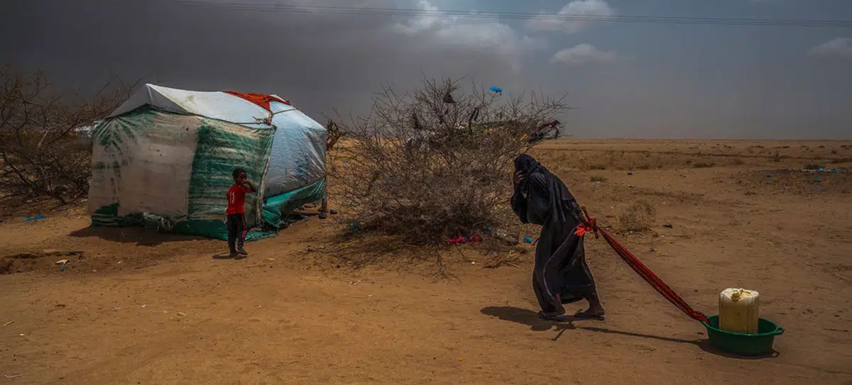 Idosa leva água para sua tenda em um campo de deslocados no norte do Iêmen, perto da fronteira com a Arábia Saudita